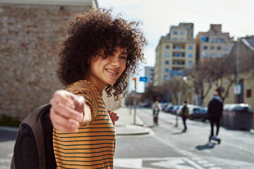 Cute young woman outstretching her arm outdoors