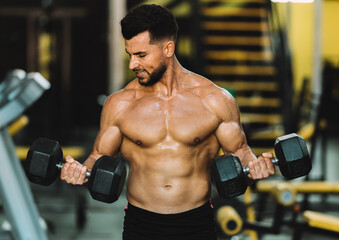 Fototapeta na wymiar Strong man raising metallic dumbbells in a gym