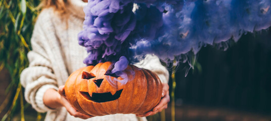 Woman holding Halloween pumpkin. Halloween orange pumpkin smoking with purple smoke.