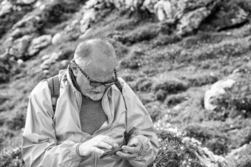 Elderly man along a mountain trail wearing eyeglasses and looking at his smartphone.