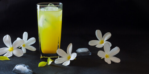 Fresh orange juice served in a glass and filled with ice and isolated on black background. Sweet,flavoured,cold,refreshing,tropical fruit juice. Front,direct view of the drink with flowers.Copy space.