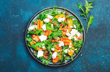 Grilled peach salad with feta cheese, hazelnuts and arugula on blue background, top view, copy space