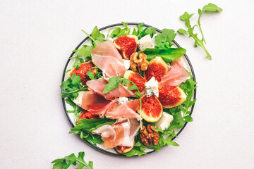 Sweet fig salad with jamon, blue cheese, walnuts, arugula on white background, top view, copy space