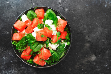 Watermelon salad bowl with soft goat cheese, spinach and pea sprouts on gray background, top view, copy space