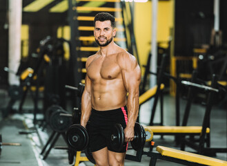 Fototapeta na wymiar Portrait of a fit man holding dumbbells in a gym