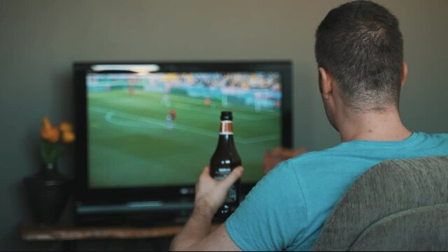Man with bottle of beer watching football on TV.