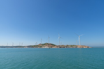 On the island in the middle of the sea, many wind turbines are installed under the blue sky