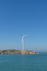 On the island in the middle of the sea, many wind turbines are installed under the blue sky