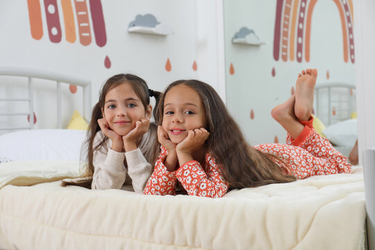 Cute girls in pajamas on bed at home