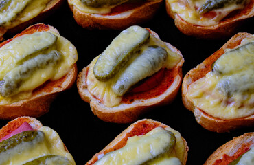 Hot sandwiches of white bread, ham, pickles and cheese on a black baking sheet