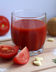Fresh tomato juice in a glass with tomatoes, salt, garlic and herbs on a wooden board