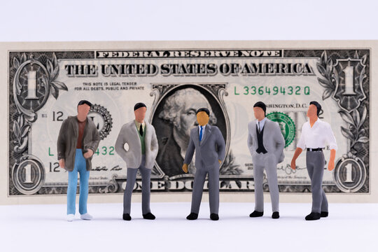 Plastic figurines of men from various social groups on the background of the one American dollar bill