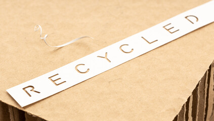 Recycled paper or cardboard concept. Die cut label of paper with text Recycled on brown cardboard