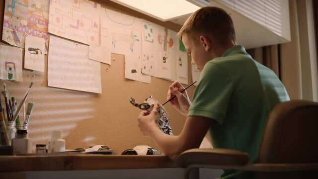Little boy focused on work. Painting robot skeleton in his room