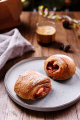 Puff pastry rolls with fruit and coffee on wooden table against Christmas tree. Danish pastries. Christmas breakfast