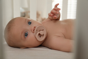 Cute little baby with pacifier lying in crib