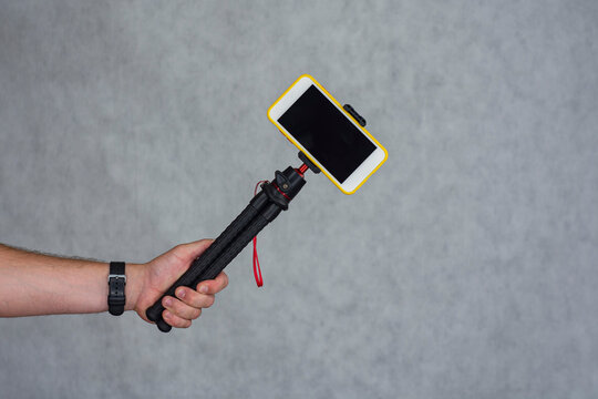 A man holds a flexible tripod with a mock-up of a smartphone with a black screen.