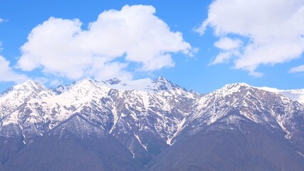 Fototapeta premium picturesque landscape of snow-capped mountains with white clouds on a blue sky on a sunny day at Krasnaya Polyana in Sochi, Russia