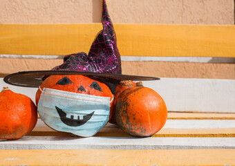 Three pumpkins, one of which has a witch hat and a medical mask with a painted scary smile. On a...