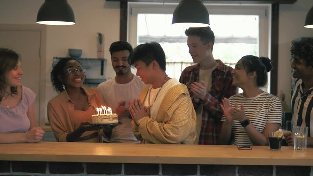Happy asian chinese teenager having birthday, blowing candles from the birthday cake, making a wish, getting a gift, celebrating with many multicultural friends