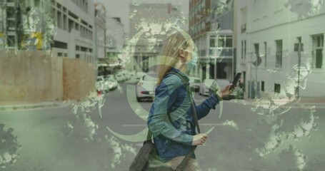 Animation of virus cells and biohazard sign over caucasian woman wearing face mask