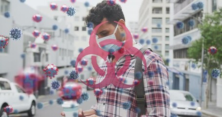 Animation of virus cells and biohazard sign over caucasian man wearing face mask