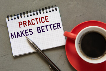 PRACTICE MAKES BETTER - words in a white notebook on a gray background with a pen and a cup of coffee