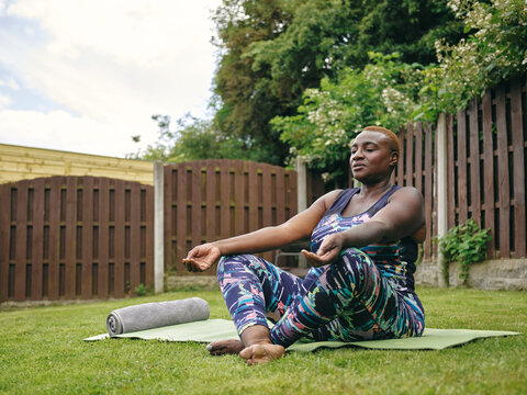 Woman meditating on yoga mat in backyard