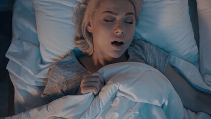 Top view of young woman snoring while sleeping on bed