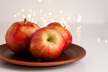 Close up of red yellow apples with water drops on the dark brown plate on bright background with yellow gold bokeh. Healthy organic food, autumn mood and still life concept with copy space