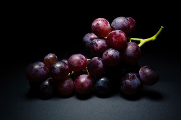 Purple grapes with green stem, wet and shiny, on black background with light coming from above