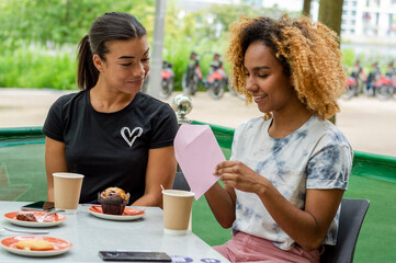 Woman opening envelope while sitting in cafe with her friend
