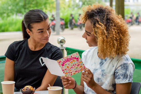 Woman Reading Birthday Card While Sitting In Cafe With Her Friend