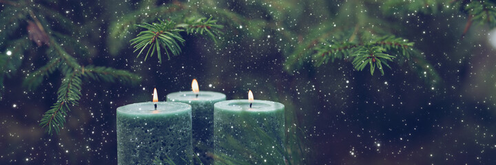 Three burning candles with snowflakes in front of a fir tree. Horizontal winter background with...