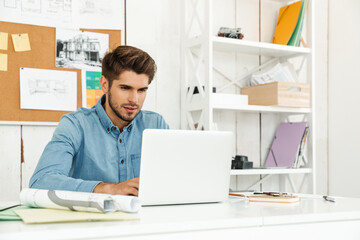 Fototapeta na wymiar Young brunette man working with laptop while sitting at desk in office