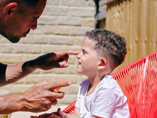 Father applying sun cream on sons face outdoors