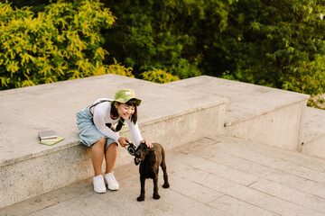 Young asian woman in hat smiling while walking with her dog