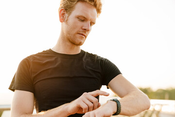 Ginger sportsman using smartwatch while working out on bridge