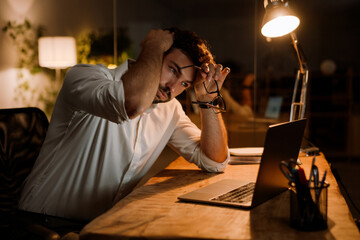 Brunette man wearing shirt working with laptop while sitting at desk