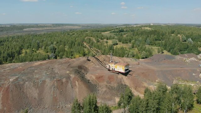 The yellow dragline makes a full turn in the movement and pours the ore out of the bucket. Summer is sunny weather. A quarry for open-pit mining.
