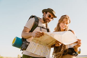 White couple with backpacks examining map while hiking together outdoors