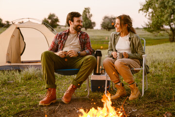 White couple smiling and drinking tea during camping together