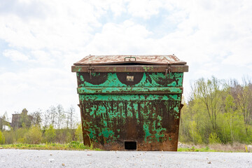 Alter, grüner, verbeulter und mit Rost überzogener Container steht auf einer Freifläche. Verschiedene Ansichten.