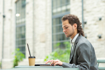 Young successful caucasian businessman works in an outdoor cafe using a computer. Business, freelance and remote work.