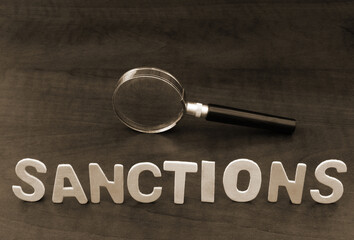 Sanctions review concept. Magnifying glass and word sanctions on wooden background. 
