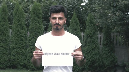 Afghan lives matter sign. The 
 muslim afghan man is holding a sign to save Afghanistan. A piece of paper request to pray for Afghanistan