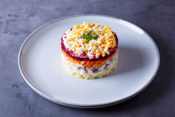 Herring salad under a fur coat. Traditional Russian multilayered salad from herring, beets, potatoes, carrots and eggs. Close-up, grey background.