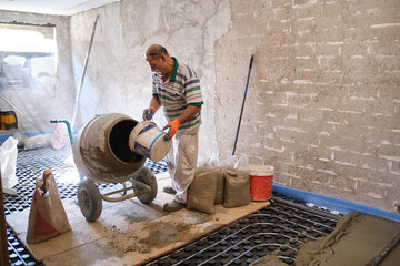 Construction worker with a bucket in his hands loads a concrete mixer.
