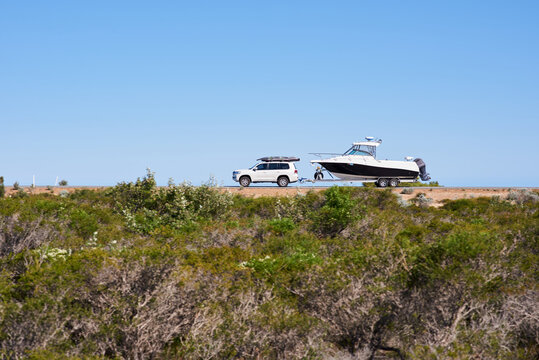 Car towing a boat along a coastal road in Western Australia under blue sky, with motion blur.