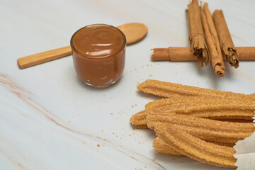 Traditional churros with sugar and cinnamon served on a marble table, with a bowl of caramel.